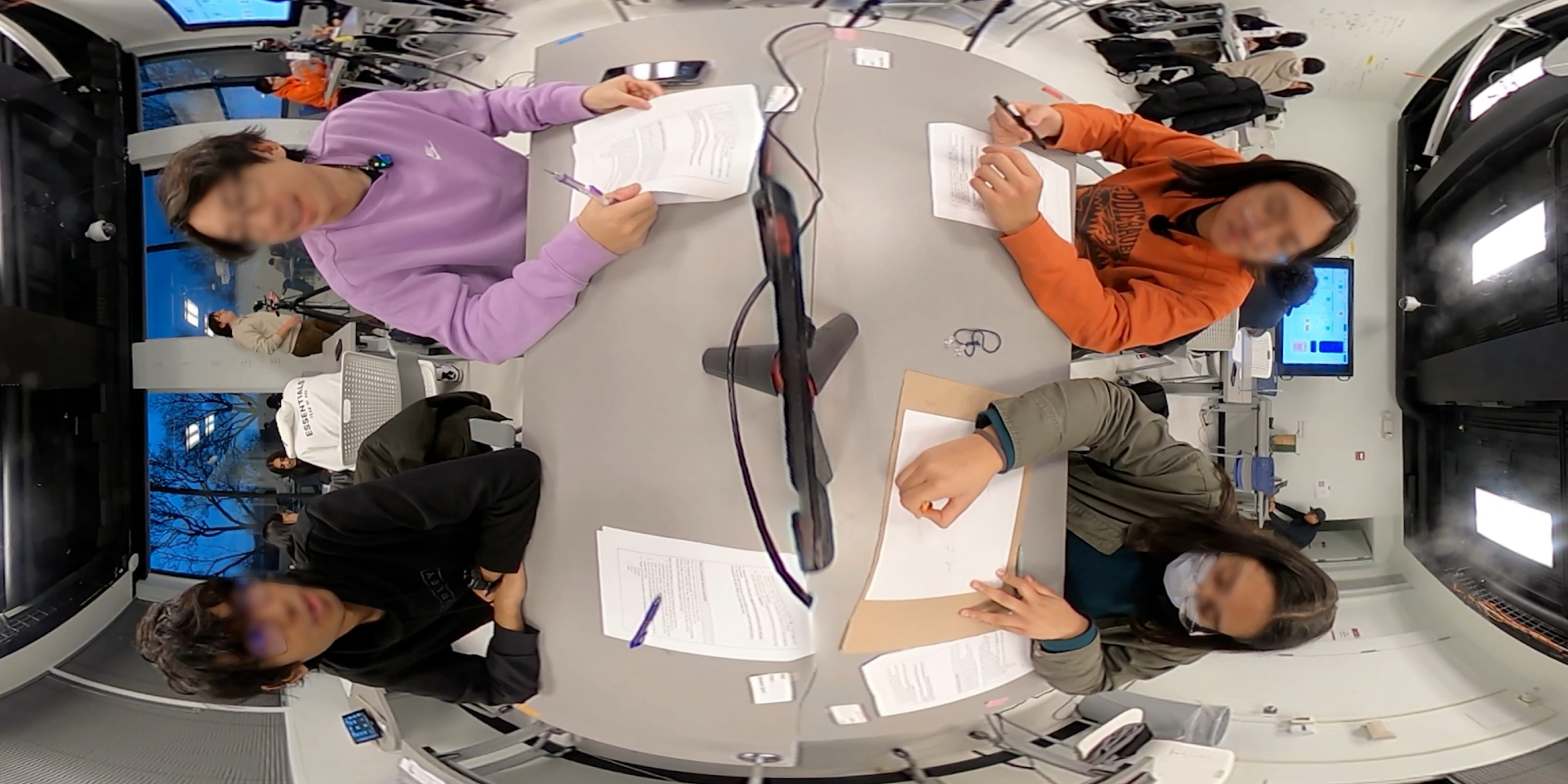 Top-down classroom frame with faces obscured, showing students positioned around a shared workspace.