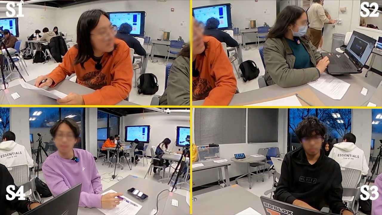 Front-facing classroom frame with faces obscured, showing two students sharing a laptop at the table.